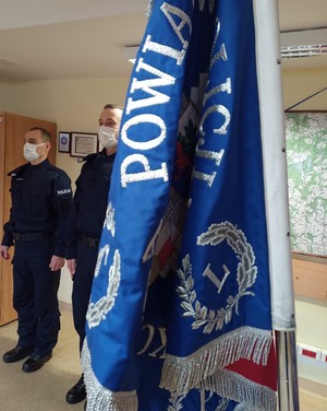 dwóch policjantów stoi za sztandarem Komendy Powiatowej Policji w Goleniowie