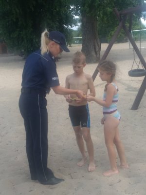 umundurowana funkcjonariuszka Policji rozdaję ulotki dzieciom na plaży