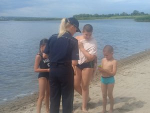 Umundurowana funkcjonariuszka Policji rozdaję ulotki dzieciom na plaży.